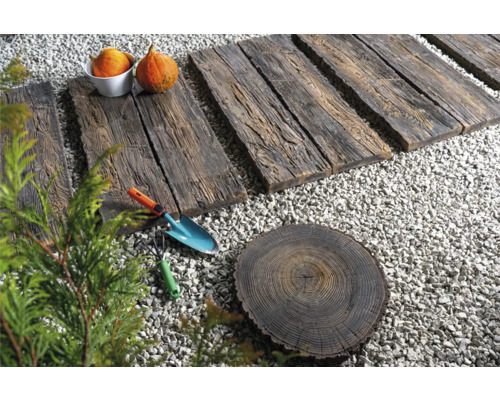 Gartenszene mit Holzwegplatten, Kies, Baumstumpfscheibe, Schaufel, Harke und Kürbissen.