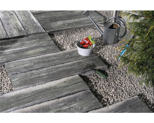 Gartenszene mit Gehwegplatten in Holzoptik, Kies, Gießkanne und Gartengeräten