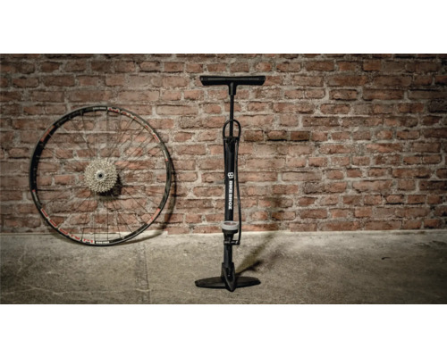 Fahrradpumpe neben einem Fahrradrad vor einer Ziegelwand