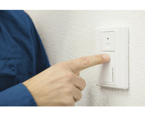 Une personne actionne un interrupteur mural Chamberlain pour ouvre-porte de garage.