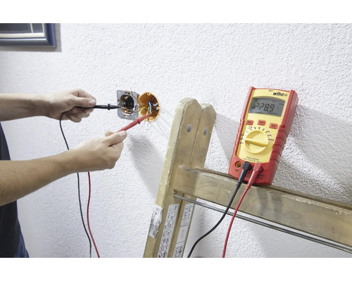 Eine Person misst mit einem Multimeter die Spannung einer Steckdose.