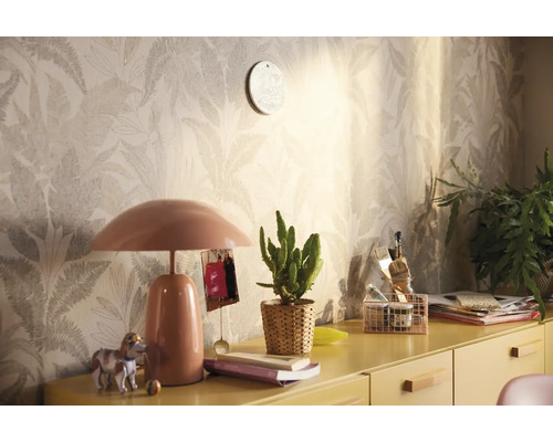 Dekoratives Zimmer mit gemusterter Tapete, Tischlampe und verschiedenen Dekorationsgegenständen auf einem gelben Schrank.