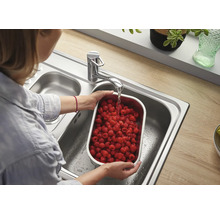 Frau wäscht Himbeeren in Edelstahlschale unter Wasserhahn in Edelstahlspüle
