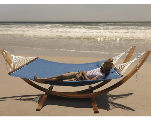Un homme se détend dans un hamac bleu avec cadre en bois sur la plage