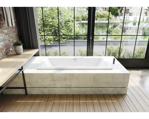 Freistehende Badewanne aus Acryl auf Betonpodest vor großem Fenster