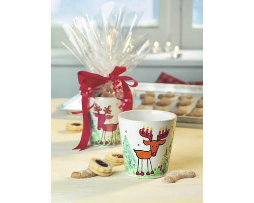 Gobelet décoratif avec motif de renne et emballage cadeau sur une table avec des biscuits.