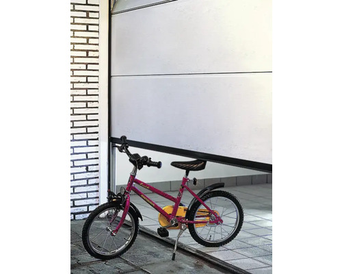 Une porte de garage blanche partiellement ouverte avec un vélo d''enfant devant.