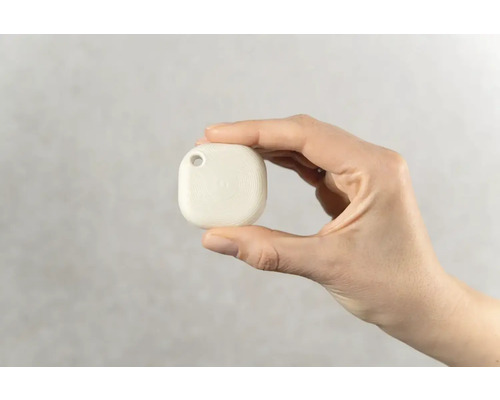 Hand hält einen weißen Ortungsanhänger mit Loch zur Befestigung