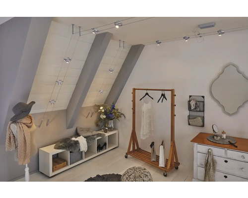 Chambre mansardée avec portant, commode, banc et système de câbles avec projecteurs pour l''éclairage.