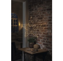 Dekorativer Stern mit LED Beleuchtung, hängend an einer Backsteinwand über einem kleinen Tisch mit Dekoration.