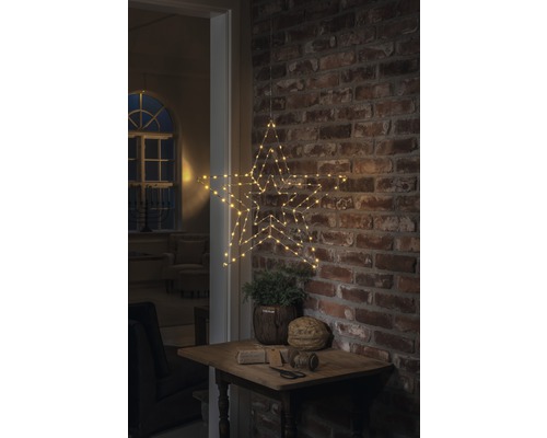 Dekorativer Stern mit LED Beleuchtung, hängend an einer Backsteinwand über einem kleinen Tisch mit Dekoration.