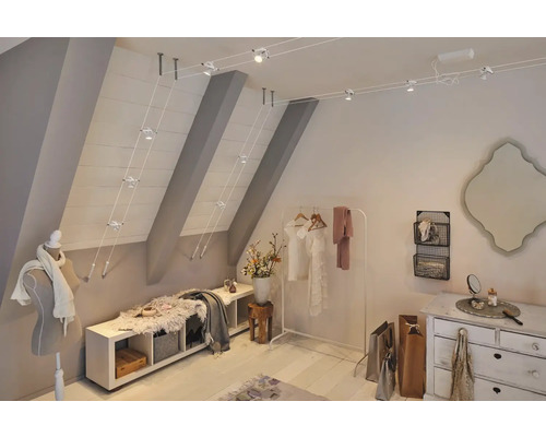 Ein Dachzimmer mit Kleiderständer, Kommode und Seilsystem Leuchte.