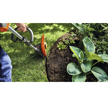 Une personne coupe les bordures de pelouse avec un coupe-bordures dans un jardin.