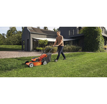 Un homme tond la pelouse avec une tondeuse Husqvarna dans un jardin devant une maison.