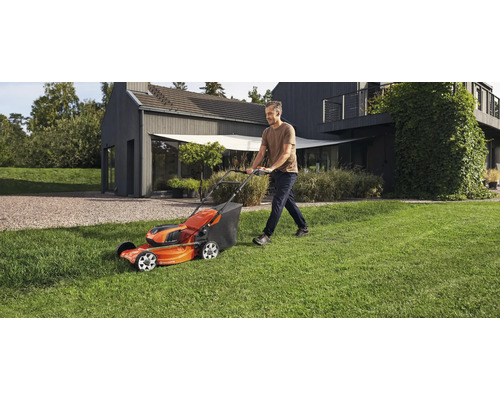 Un homme tond la pelouse avec une tondeuse Husqvarna dans un jardin devant une maison.