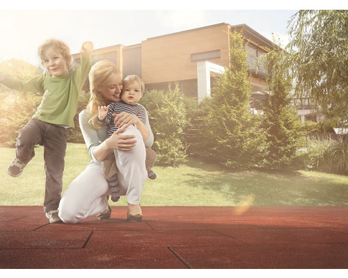 Mutter mit Kindern auf dem Spielplatz mit Fallschutzmatten vor Haus und Garten
