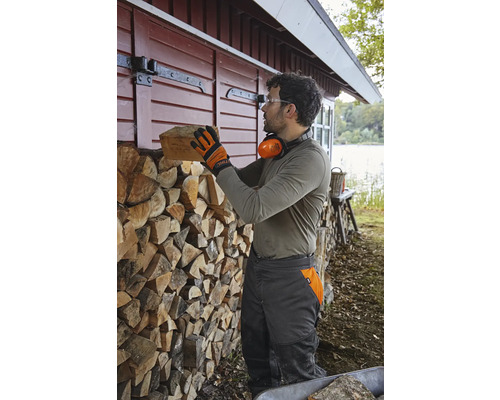 Mann stapelt Brennholz an einer Holzwand neben einem Haus.
