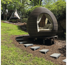 Scène de jardin avec un lit d''extérieur rond et couvert et un hamac sur une colline verdoyante