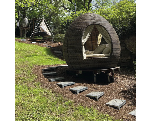 Gartenszene mit einem runden, überdachten Outdoor-Bett und einer Hängematte auf einem grünen Hügel