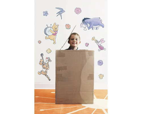 Garçon dans une boîte en carton devant un mur avec des autocollants muraux Winnie l''ourson