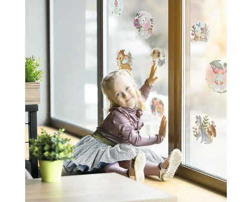 Mädchen spielt mit Fensteraufklebern mit Tiermotiven auf einer Fensterscheibe.