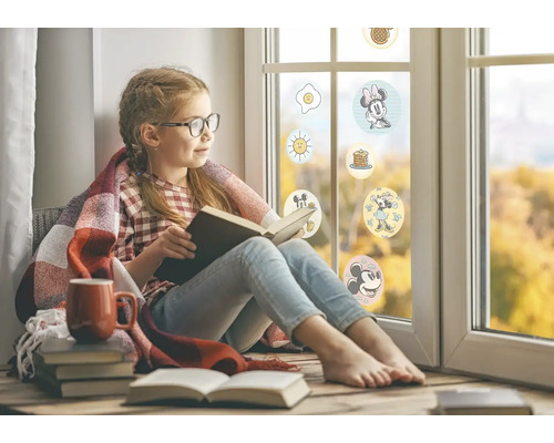 Mädchen liest Buch am Fenster mit Disney-Aufklebern