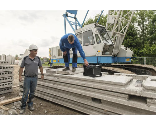 Deux ouvriers du bâtiment avec une radio de chantier et des éléments préfabriqués en béton devant une grue