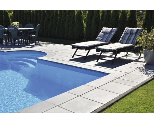 Scène avec piscine, terrasse avec dalles en pierre, chaises longues et table de jardin avec chaises.
