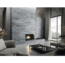 Salon avec cheminée, canapé, table et mur carrelé aspect béton.