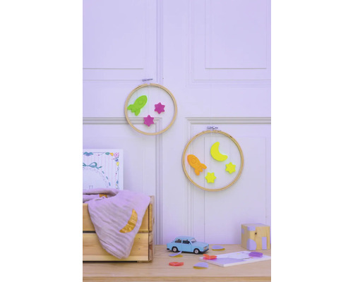 Dekorative Kinderzimmer Szene mit Stickrahmen, Raketen, Sternen, Halbmond, Spielzeugauto und Holzkiste auf einem Tisch vor einer Wand