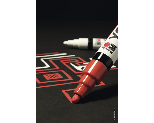 Marqueur laque rouge dessinant un motif sur fond noir, avec un autre marqueur en arrière-plan.