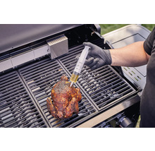 Une personne injecte du liquide avec une seringue dans un poulet grillé sur un barbecue.