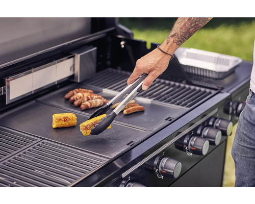 Person grillt Mais und Würstchen auf einem Grill.