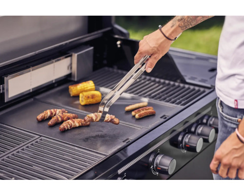 Une personne grille des saucisses, du lard et des épis de maïs sur un barbecue.