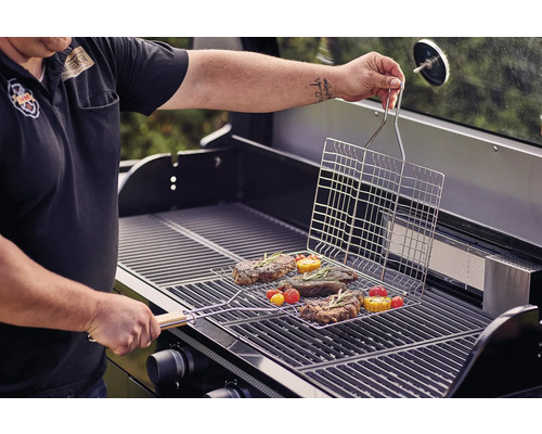 Une personne grille des steaks et des légumes avec un panier à griller sur un barbecue à gaz.