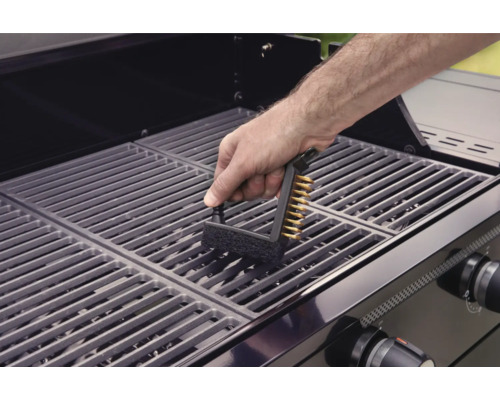Une personne nettoie une grille de barbecue avec une brosse à barbecue.