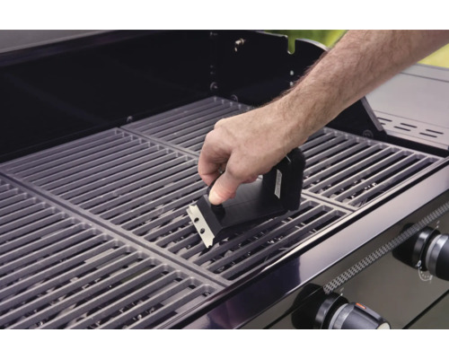 Une personne nettoie une grille de barbecue avec une brosse de barbecue.