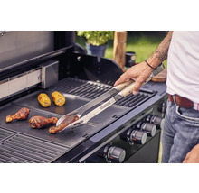 Un homme fait griller des pilons de poulet et des épis de maïs avec une pince à griller sur un barbecue