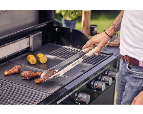 Un homme fait griller des pilons de poulet et des épis de maïs avec une pince à griller sur un barbecue