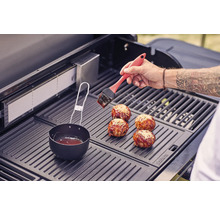 Une personne badigeonne des boulettes de viande avec un pinceau sur un gril.