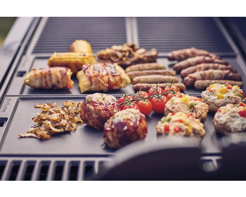 Verschiedene Speisen wie Würstchen, Speck, Tomaten und gefüllte Champignons auf einem Grill.