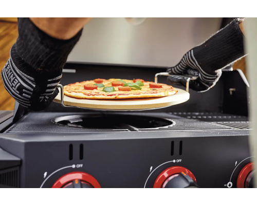 Une pizza sur une pierre à pizza est poussée dans un barbecue à gaz