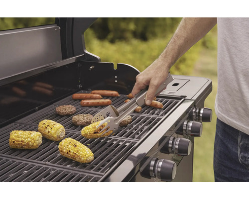 Grill mit Grillgut wie Maiskolben, Würstchen und Burger-Patties, eine Person benutzt eine Grillzange.