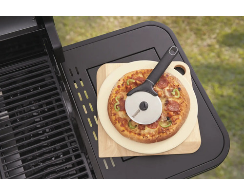 Pizza auf Holzbrett mit Pizzaschneider neben einem Grill