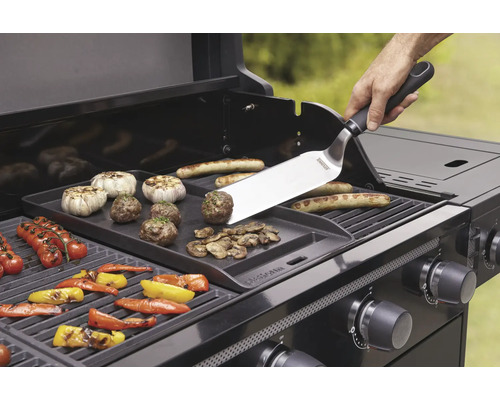 Grill mit Grillplatte, Grillbesteck und verschiedenen Lebensmitteln wie Gemüse, Würstchen und Fleischbällchen