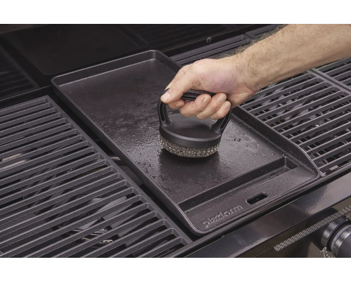 Une plaque de gril est nettoyée avec une brosse pour gril.