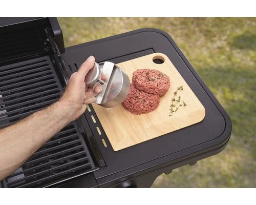 Eine Person formt mit einer Burgerpresse Burgerpatties auf einem Schneidebrett neben einem Grill.