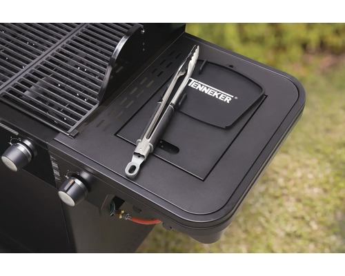 Detailansicht eines schwarzen Gasgrills mit Grillzange auf der Seitenablage und Tenneker Logo.
