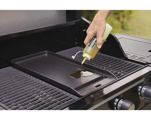 Une personne verse de l''huile sur une plaque de gril sur un barbecue à gaz.
