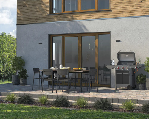 Terrasse avec table de jardin, chaises et barbecue devant une maison.